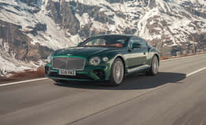 綠色 Bentley 跑車在白雪覆蓋的山峰的山路上行駛。 — MacBook Pro M1 壁紙