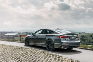 灰色ABT Audi A5 Sportback停泊在風景優美的鄉村道路上，有山丘和長椅。 — Surface Pro 壁紙