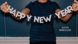 一個人手持白色Happy New Year橫幅，帶有2023 MMXXIII文字，在藍色牆壁上。