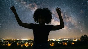 一個人在城市上空的星空下舉起雙臂。