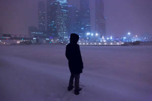 人站在雪中，面向夜晚燈火通明的城市天際線。