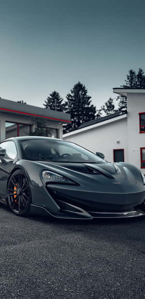 深灰色McLaren跑車停泊在帶有紅色飾邊的現代白色建築前。 — Huawei Mate 70 Air 壁紙