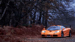 橙色McLaren F1在黃昏時停泊在森林道路上。 — 4K 法拉利 壁紙