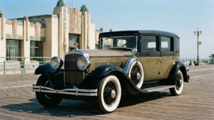 經典1930年代汽車在陽光普照的海濱長廊旁，靠近裝飾藝術風格建築