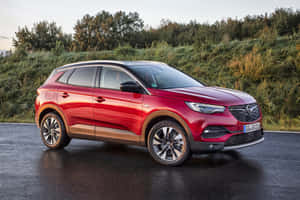 日落時紅色Opel Mokka X SUV停泊在潮濕道路旁，靠近綠色植物。 — Surface Laptop 壁紙