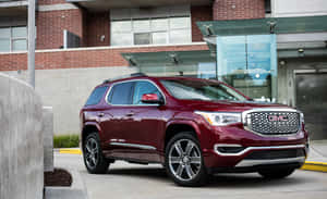 棗紅色GMC Acadia SUV停泊在現代磚和玻璃建築前。 — MacBook Air M1 壁紙
