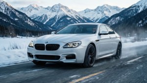 白色BMW M6轎跑在雪覆蓋的山路上行駛，背景是雪頂的山峰。