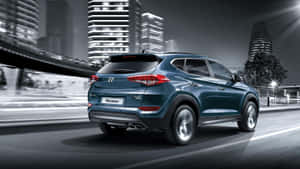 青綠色現代 Tucson SUV 在夜間城市中快速行駛，燈光和建築物模糊不清。 — 現代汽車 壁紙