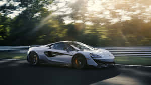 日落時分，銀色McLaren賽車在森林賽道上疾馳。 — 5120x2880 壁紙