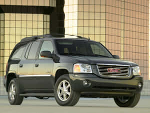 白天黑色GMC Envoy SUV停在一棟現代玻璃建築前。 — 4:3 壁紙
