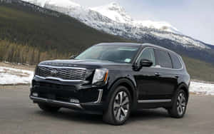 黑色Kia Telluride SUV停在雪山和常綠樹附近。 — 1280x800 壁紙