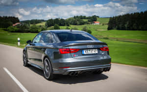 灰色Audi S3轎車在鄉村道路上行駛，周圍有綠色田野和樹木。 — Steam Deck OLED 壁紙