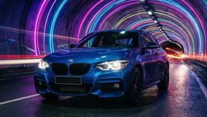 藍色BMW汽車在夜間霓虹燈照亮的隧道中飛馳。