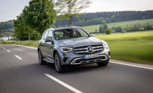 銀色 Mercedes GLC SUV 在鄉村道路上行駛，周圍有綠色田野和樹木。 — Steam Deck 壁紙