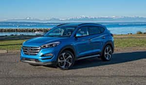藍色現代Tucson SUV停在水邊，背景有山脈。 — 現代汽車 壁紙