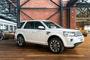 白色 Land Rover Freelander II 在磚牆汽車展廳的硬木地板上。 — MacBook Air M4 壁紙