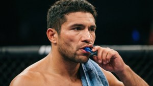 MMA拳手在八角籠中咬著護齒，毛巾搭在肩上。