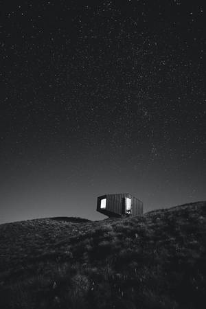 星空夜空下，山丘上的一座現代小屋，窗戶閃閃發光。