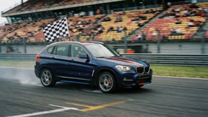 藍色BMW X3 SUV在賽車場上衝過終點線，帶有格子旗。