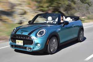 一輛青綠色的MINI Cooper S開篷跑車在陽光明媚的道路上行駛，車內有司機。 — MacBook Air 13 壁紙