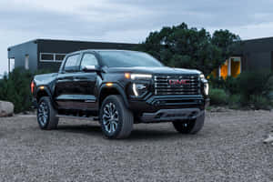 黑色GMC Sierra Denali皮卡車在黃昏時停泊在現代房屋附近的碎石路上。 — Surface Pro 壁紙
