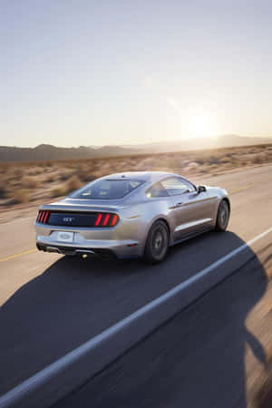 銀色Mustang GT在金色日落時分於沙漠高速公路上飛馳。 — Vivo Pad 壁紙