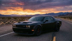 日落時分沙漠公路上的黑色Dodge Challenger Hellcat，背景有山脈。