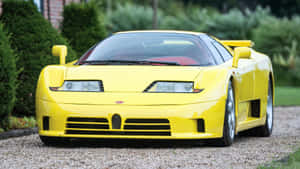 黃色 Bugatti EB110 Super Sport 停泊在碎石上，背景有綠色灌木。 — 布加迪 壁紙