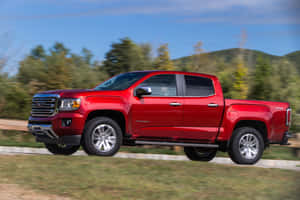 紅色GMC Canyon皮卡車在風景如畫的道路上行駛。 — 3:2 壁紙