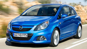 藍色Opel Corsa在陽光明媚的道路上行駛，背景模糊。 — 霓虹紅美學 壁紙
