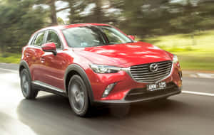 紅色Mazda CX-3 SUV在陽光明媚的道路上快速行駛，周圍有綠色樹木。 — Steam Deck OLED 壁紙