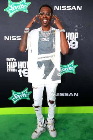 穿著白色破洞牛仔褲和眼鏡的男子在BET Hip Hop Awards的綠色地毯上微笑。