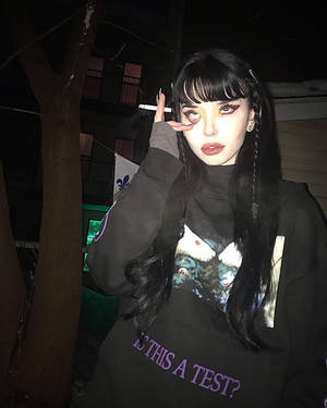 深色頭髮、妝容大膽的年輕女性在夜晚拿著香煙。