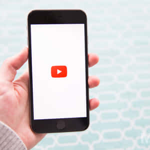 手拿著智能手機，白色屏幕上顯示YouTube應用程式圖標。 — YouTube 壁紙