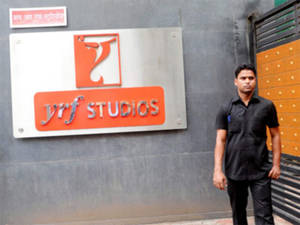 男子站在灰色牆壁上的YRF Studios標誌前