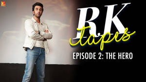 Ranbir Kapoor 身穿白色外套和牛仔褲，交叉雙臂站在「RK Tapes」文字旁。