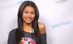 Zendaya 在品牌活動中穿著休閒露肩T恤對著鏡頭微笑。 — 禪 壁紙