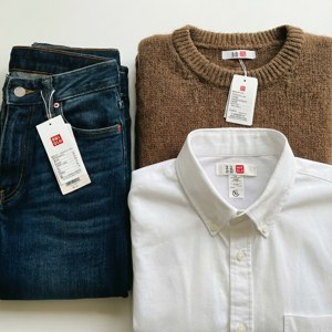 三件摺疊的Uniqlo衣物，包括牛仔褲、毛衣和襯衫，標籤可見。 — Galaxy Watch 壁紙