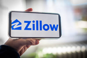手拿著顯示 Zillow 房地產應用程式標誌的手機
