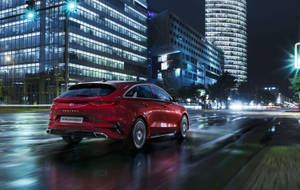 紅色Kia Proceed旅行車在雨夜城市中行駛，燈光閃爍。