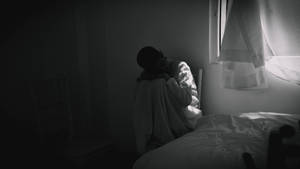 一個人裹著毯子，蜷縮在昏暗房間的窗邊。