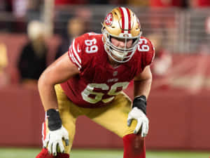 身穿紅金色球衣的美式足球員在比賽中蹲伏在球場上。 — NFL 美式足球 GIF 壁紙