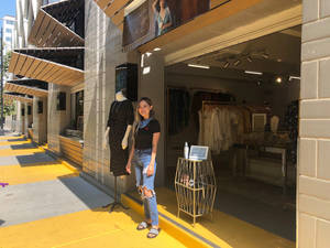 女士在黃色行人路和模特兒公仔的服裝店外微笑。