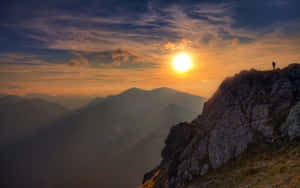 一個人站在岩石山頂，觀看日落於層層疊疊的山脈之上。