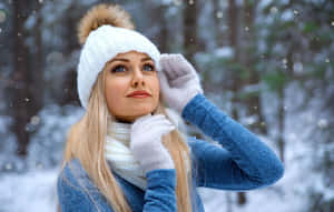 穿著冬季服裝的女性站在雪地森林中仰望飄落的雪。 — 冬日美學 壁紙