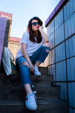 年輕女性戴著太陽眼鏡，穿著破洞牛仔褲，坐在城市混凝土台階上。 — 女孩 壁紙