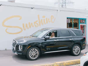 黑色SUV中的女子在帶有「Sunshine」壁畫的牆旁微笑。 — 酷車 壁紙