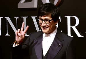 身穿西裝和眼鏡的男子在週年活動中微笑並做出和平手勢。 — 胡桃 壁紙