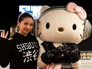 黑帽衫女性在戴著耳機和蕾絲服裝的巨型Hello Kitty吉祥物旁邊揮手。 — 東京喰種角色 壁紙