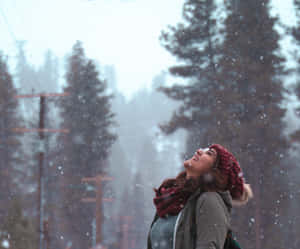 女性在飄雪中戴著紅色帽子和圍巾在雪地森林中大笑 — 冬日美學 壁紙